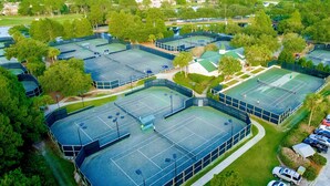 Eine Vogelperspektive auf einen Sportkomplex mit mehreren Tennisplätzen, umgeben von Grünflächen und Wohnhäusern.