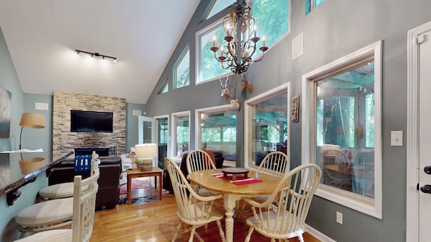 A dining area with a stone fireplace, a chandelier, and large windows. - Mountain Home Dog-friendly Getaway (Cashiers)