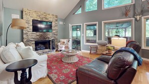 A living room with a stone fireplace, a flat-screen TV, a large window, and a leather sofa. - Mountain Home Dog-friendly Getaway (Cashiers)