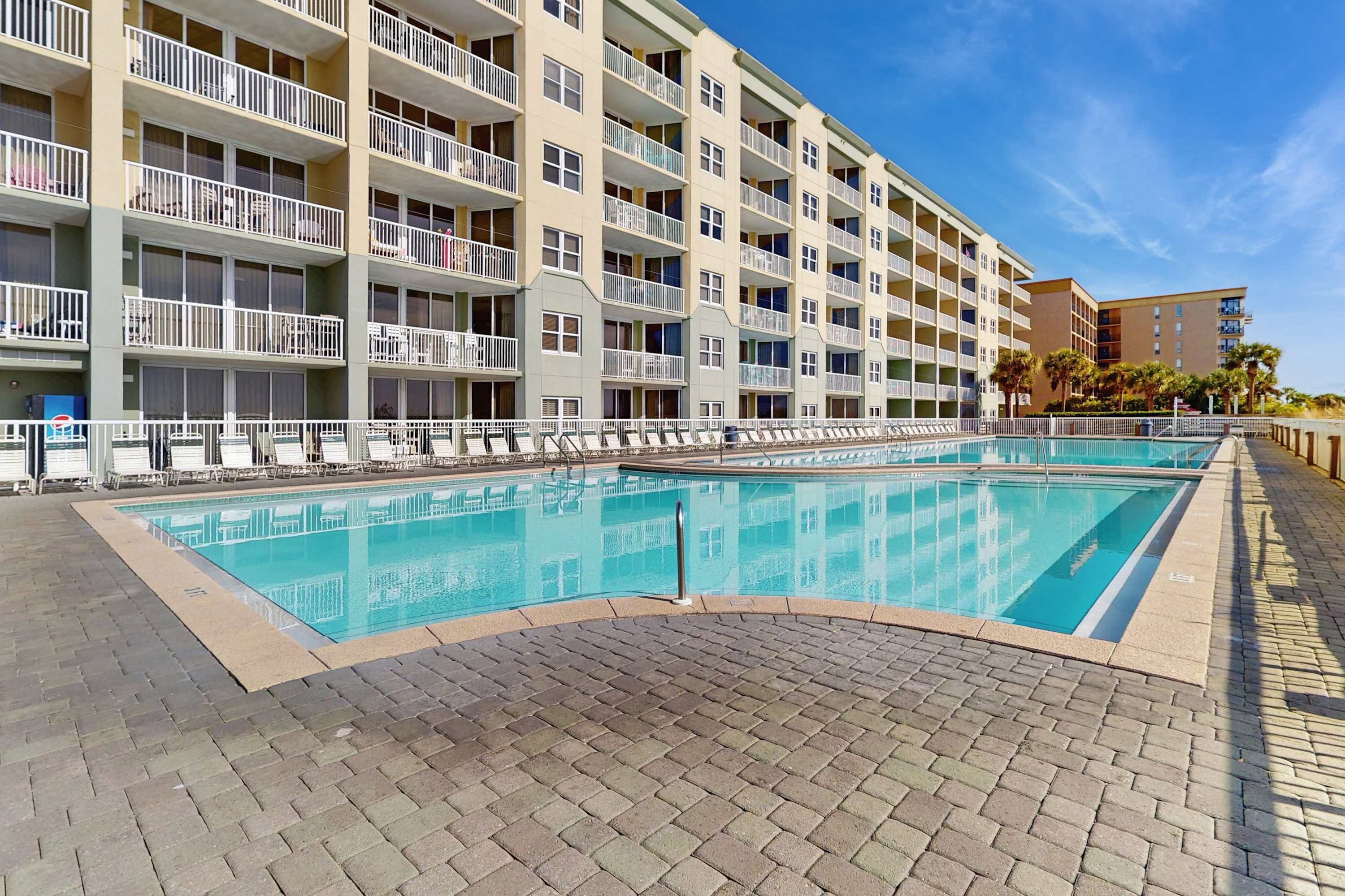 A multi-story hotel with a swimming pool, balconies, and a brick pathway.