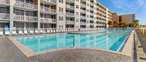 A multi-story hotel with a swimming pool, balconies, and a brick pathway.