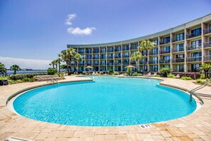 A hotel with a large circular pool, multiple balconies, and palm trees. - Cozy soundfront studio with shared pool, beach access & close to everything (Fort Walton Beach)