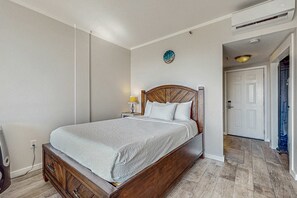 A bedroom with a wooden bed, a bedside table with a lamp, a clock on the wall, and a door leading to another room. - Cozy soundfront studio with shared pool, beach access & close to everything (Fort Walton Beach)