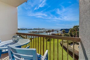 A balcony with a table and chairs, overlooking a marina with boats and a clear blue sky. - Cozy soundfront studio with shared pool, beach access & close to everything (Fort Walton Beach)