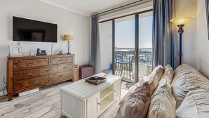 Una sala de estar moderna con una televisión de pantalla plana, un aparador de madera y un sofá con vistas a la ciudad a través de amplias ventanas.