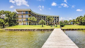 Un hotel con fachada curva, un muelle de madera que se adentra en una masa de agua y un área verde con árboles.