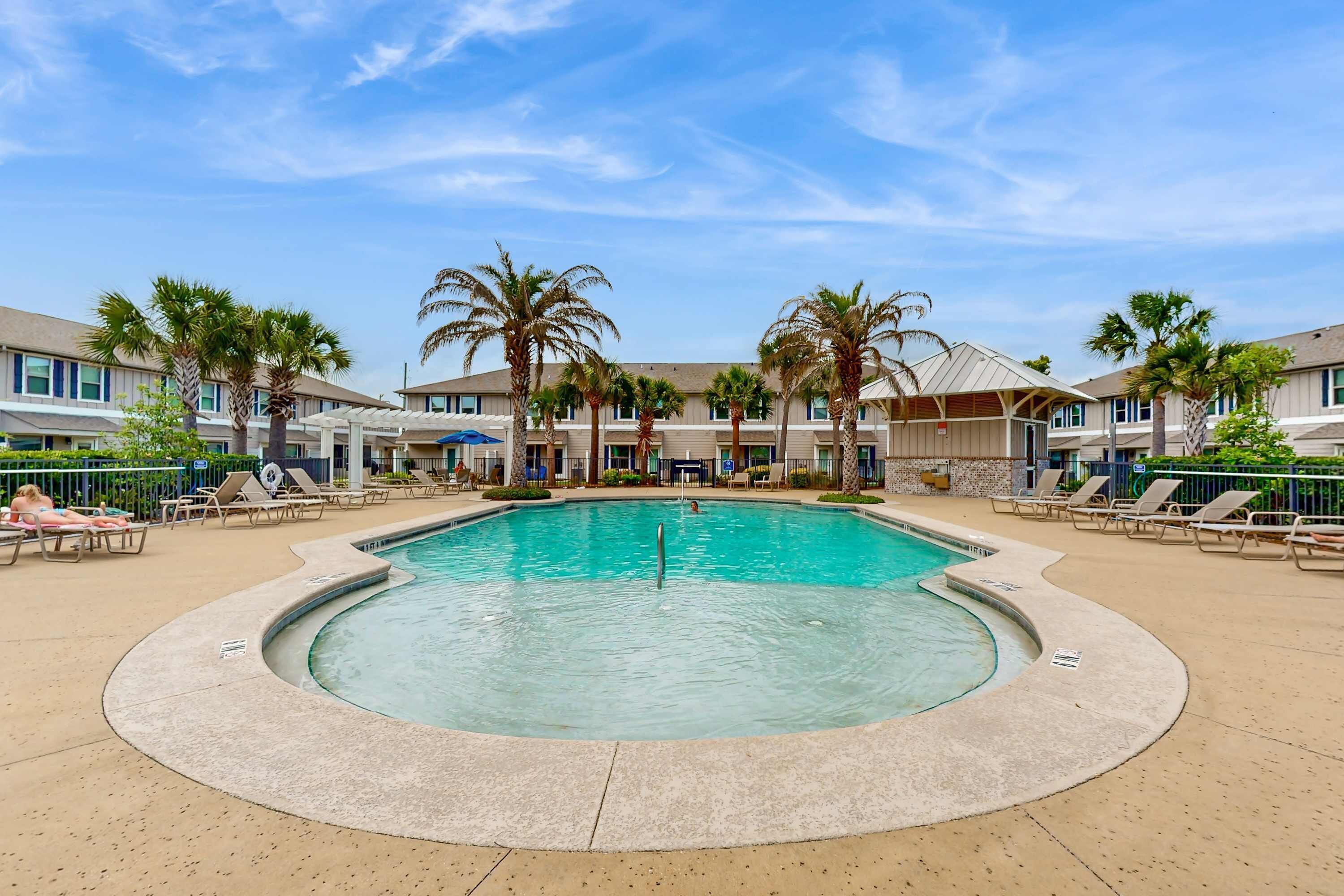 Una piscina con sillones de descanso y palmeras, rodeada de edificios de hotel.