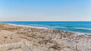 Ein Strand mit einer Holzpromenade, die zum Ufer führt, ein klarer blauer Himmel und das Meer im Hintergrund.