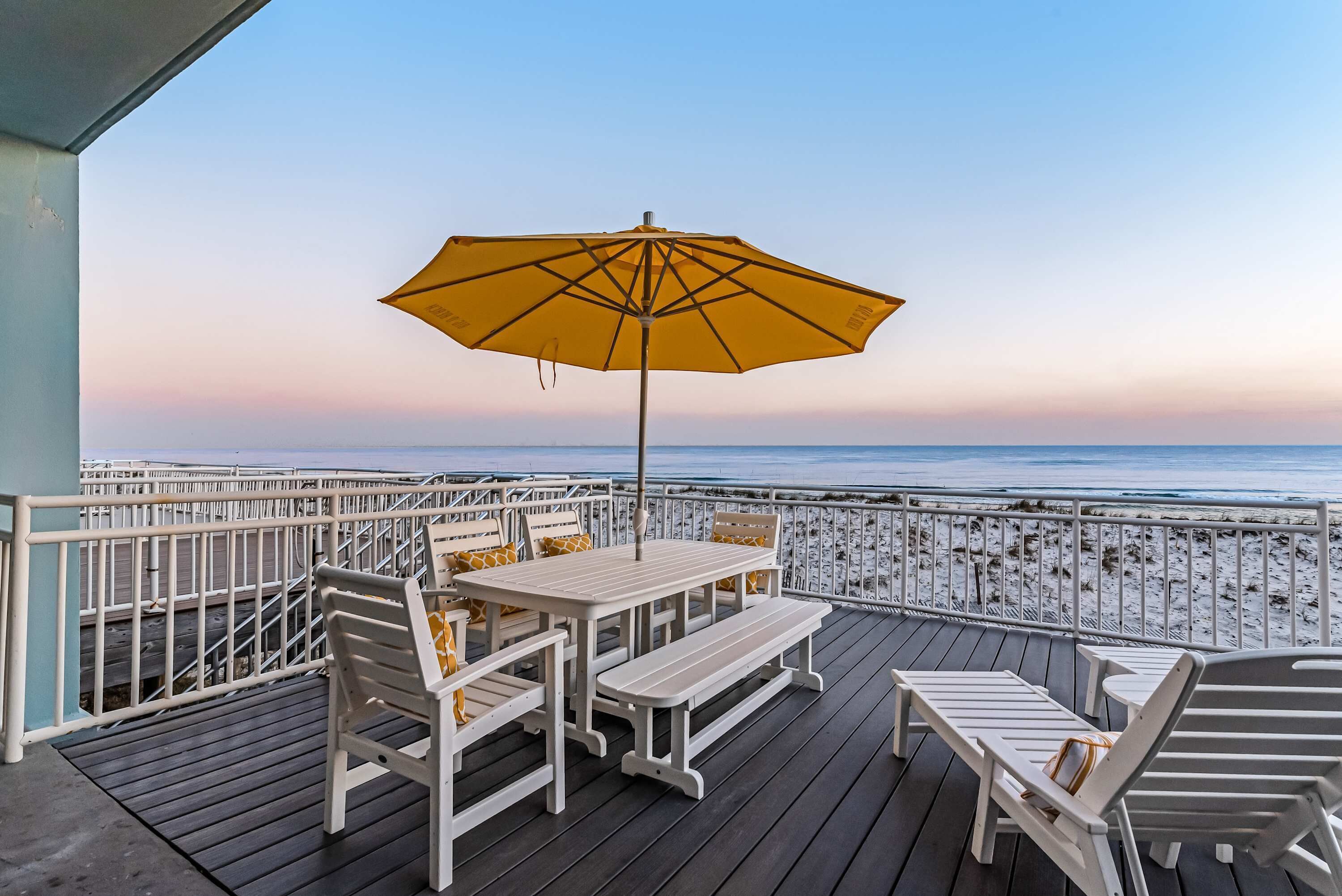 Una terraza con mesa y sillas, un paraguas y vistas a la playa.
