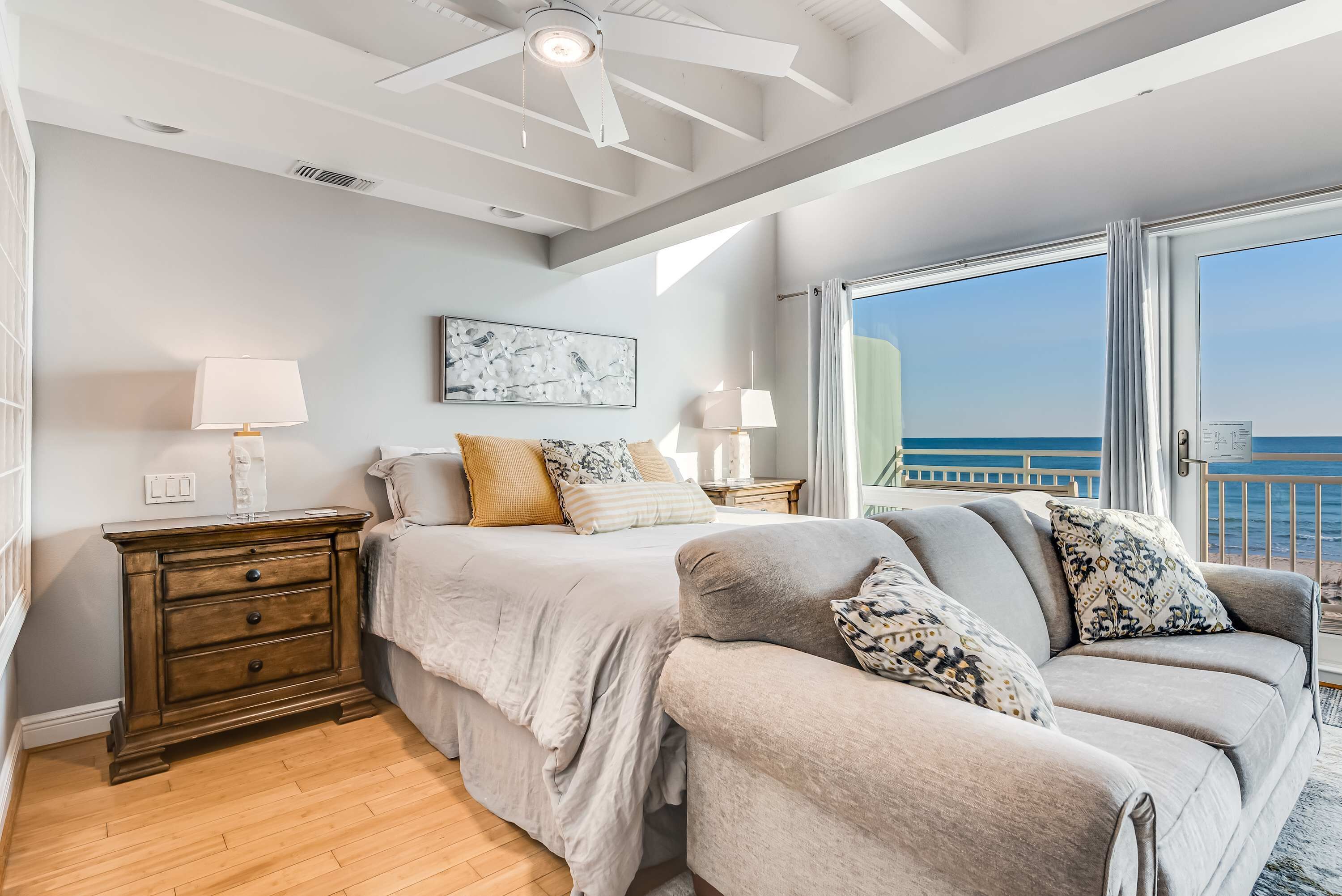 Een slaapkamer met een bed, nachtkastjes, een dressoir, een bank en een groot raam met uitzicht op zee.