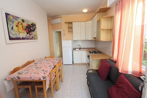 A compact kitchen with a dining table and chairs, a sofa with cushions, and a painting on the wall. - Cozy Flat With Outdoor Space (Rosolina)
