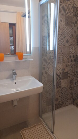 Ein Badezimmer mit einem weißen Waschbecken, einem Spiegel und einer Dusche mit gemusterten Fliesen.
