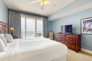 Ein Hotelzimmer mit einem großen Bett, einem Schminktisch, einem Fernseher und einem Balkon mit Vorhängen.