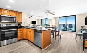 A modern kitchen with built-in appliances, a dining area with a view of the ocean, and a balcony with outdoor seating. - Gulf-Front Condo w Free WiFi & Shared Pools, Hot Tub & Sauna - Snowbird Friendly (Destin)