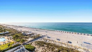 A beach with a pool area, umbrellas, and a pier. - Gulf-Front Condo w Free WiFi & Shared Pools, Hot Tub & Sauna - Snowbird Friendly (Destin)