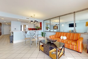 A modern living room with a sofa, a dining table, and a kitchen area in the background. - Gulf-Front Condo w Lovely Gulf View, Beach Access & Shared Pool, Hot Tub & Gym (Destin)