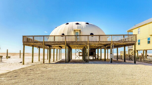 Una casa sulla spiaggia con veranda in legno e struttura a cupola.