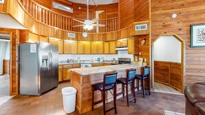 Un'ampia cucina con pareti in legno, un'isola centrale con sgabelli da bar, un frigorifero in acciaio inossidabile e una ventola a soffitto.