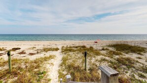 A beach with sand, grass, and a wooden structure.