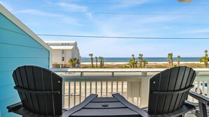 Ein Balkon mit zwei schwarzen Adirondack-Stühlen, einem weißen Geländer und Blick auf Strand und Meer.