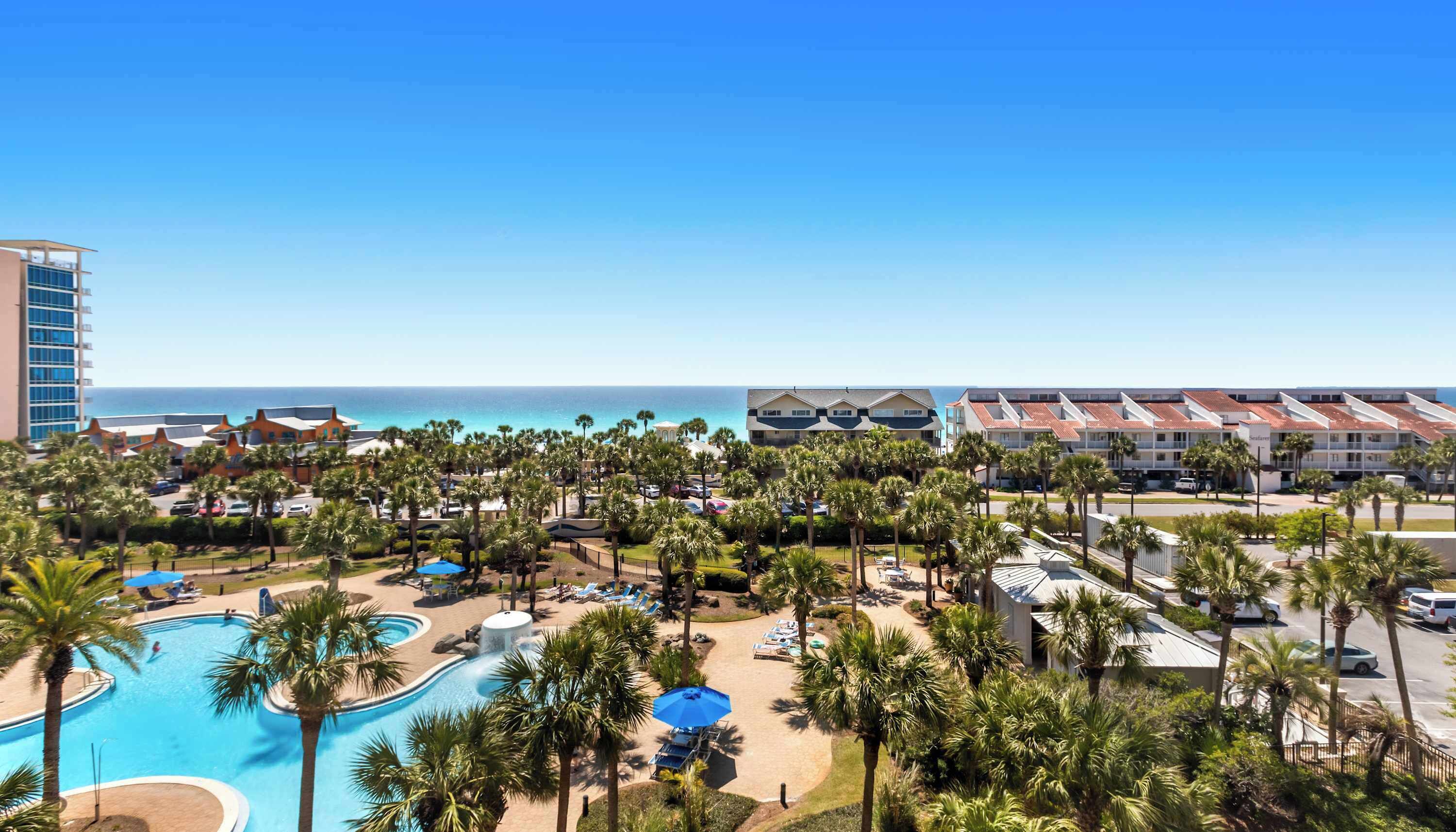 A resort with a swimming pool, palm trees, and a view of the ocean.