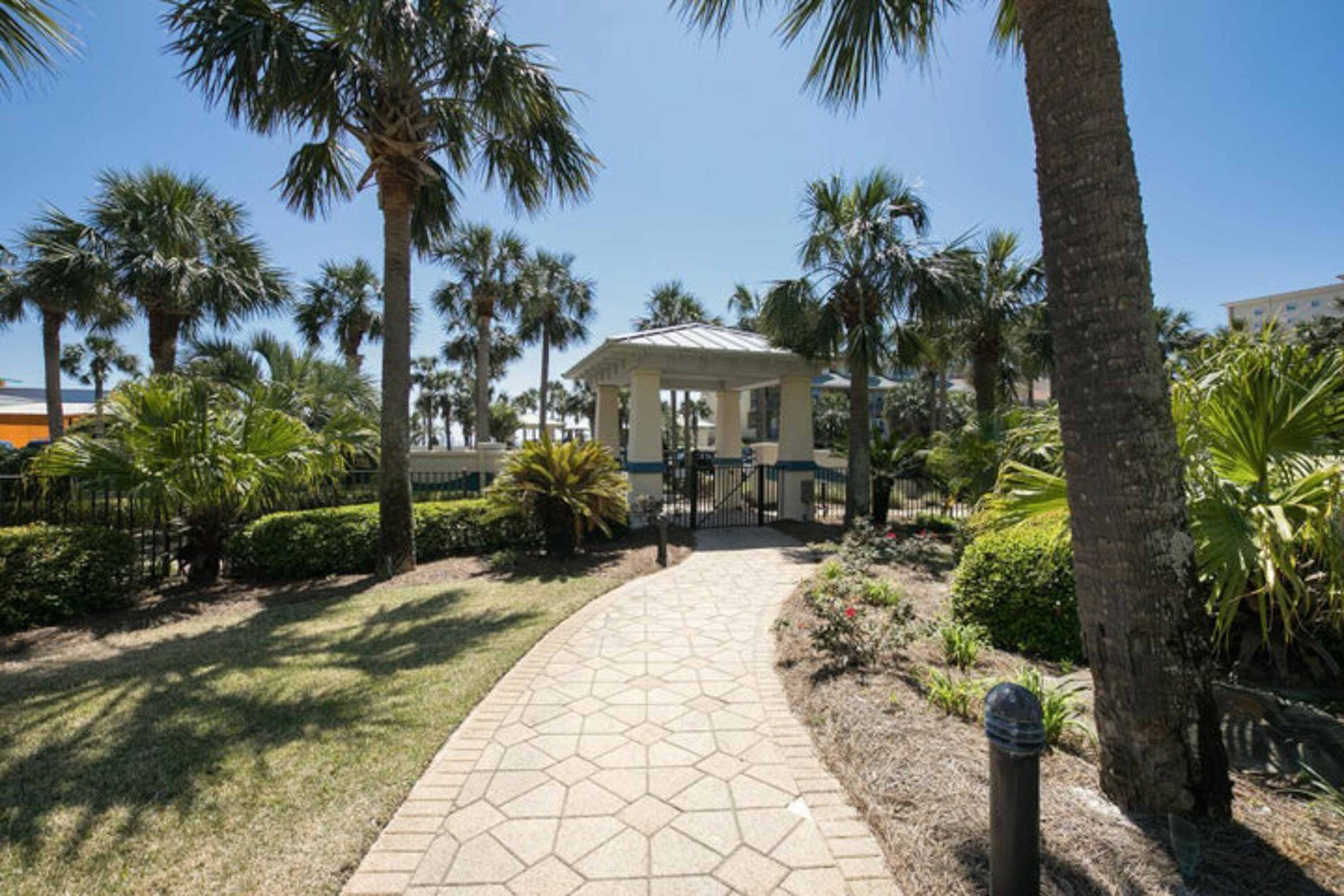 A pathway leading to a building with a dome structure, surrounded by palm trees and well-maintained landscaping.