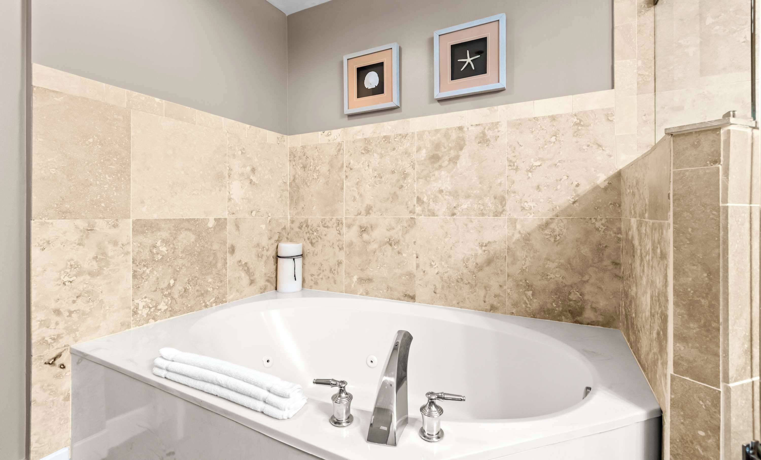 A bathroom with a bathtub, two framed pictures on the wall, and a towel rack with folded towels.