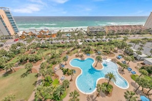 Ett semesterparadis med en stor pool formad som en björn, omgivet av palmer och med utsikt över stranden.