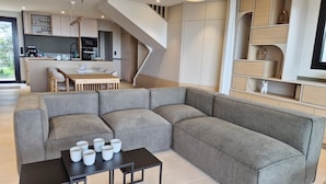 A modern living room with a sectional sofa, a black coffee table, and a kitchen area in the background. - VILLA BEAUMER - Beach Access . Sea view - TK60 (Carnac)