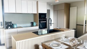 A modern kitchen with a central island, built-in appliances, and a dining area with a glass table. - VILLA BEAUMER - Beach Access . Sea view - TK60 (Carnac)