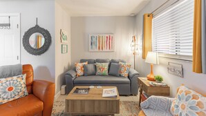 Een woonkamer met een grijze bank, een oranje fauteuil, een houten salontafel en een lamp.