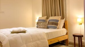 Ein ordentlich bezogenes Bett mit weißer Daunendecke, zwei Kissen mit Muster und einem gewebten Korb, sowie einem runden Teppich auf dem Boden.