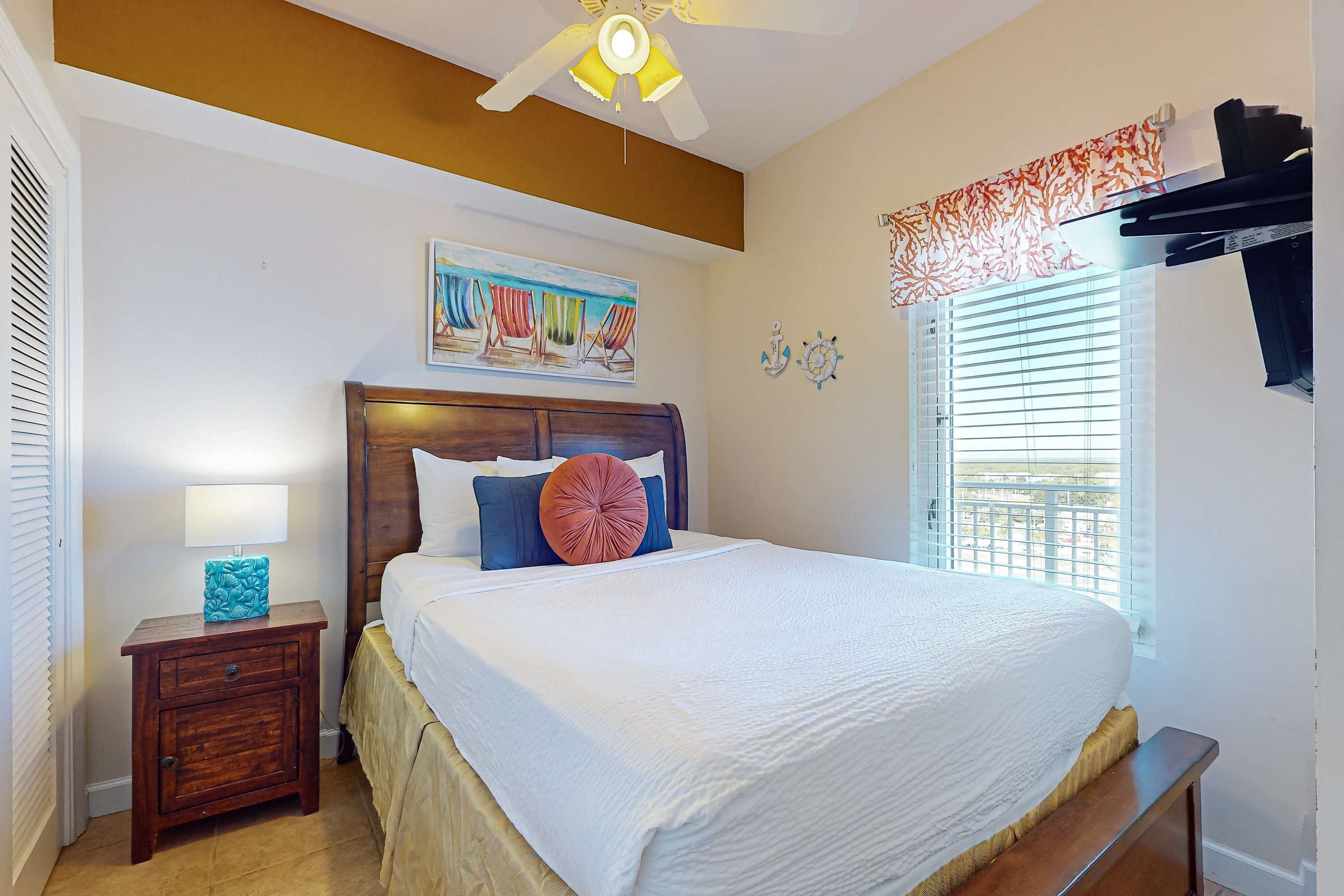 A neatly made bed with a wooden headboard, a bedside table with a lamp, and a window with blinds.