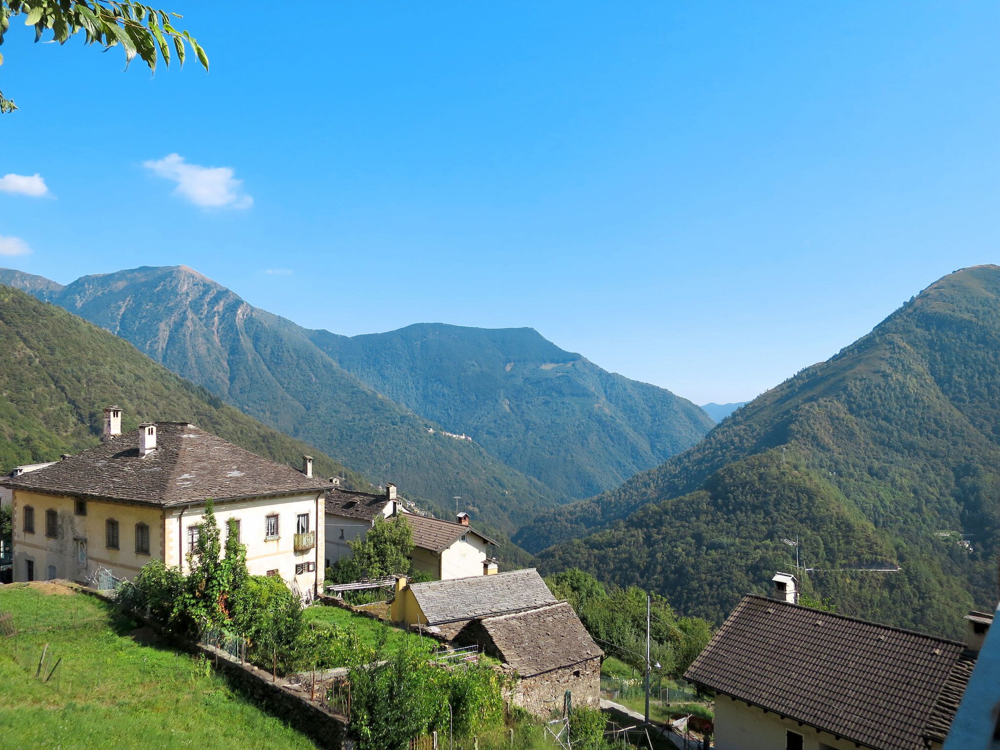 A rural village with traditional stone buildings, surrounded by lush green mountains under a clear blue sky.