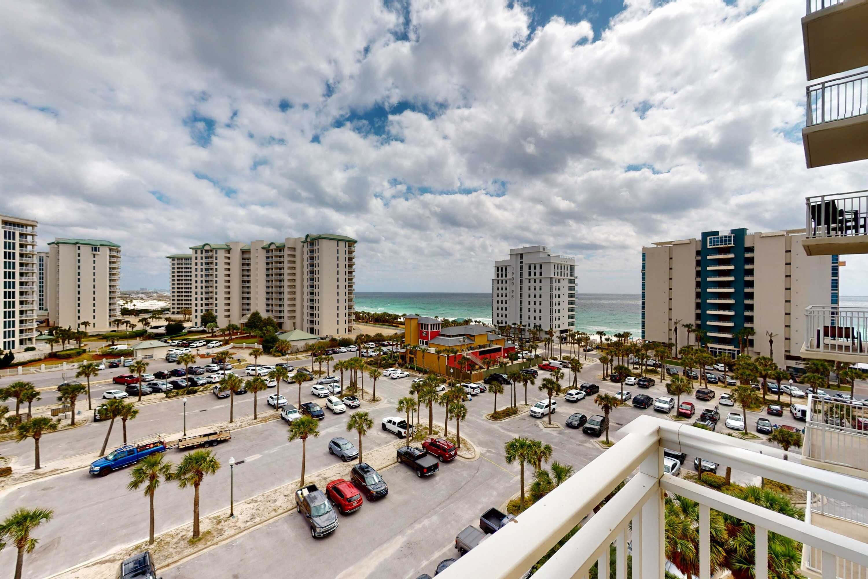 A coastal cityscape with high-rise buildings, a parking lot, and a view of the ocean.