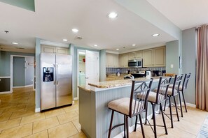 A modern kitchen with a central island, bar stools, and a microwave. - Spacious home with gorgeous gulf views, pool, large balcony, & fitness center (Destin)