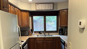Une cuisine avec des meubles en bois, un réfrigérateur blanc, une fenêtre donnant sur l’extérieur et un thermostat fixé au mur.