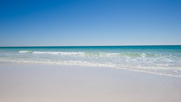 A beach with clear blue water and a sandy shore.