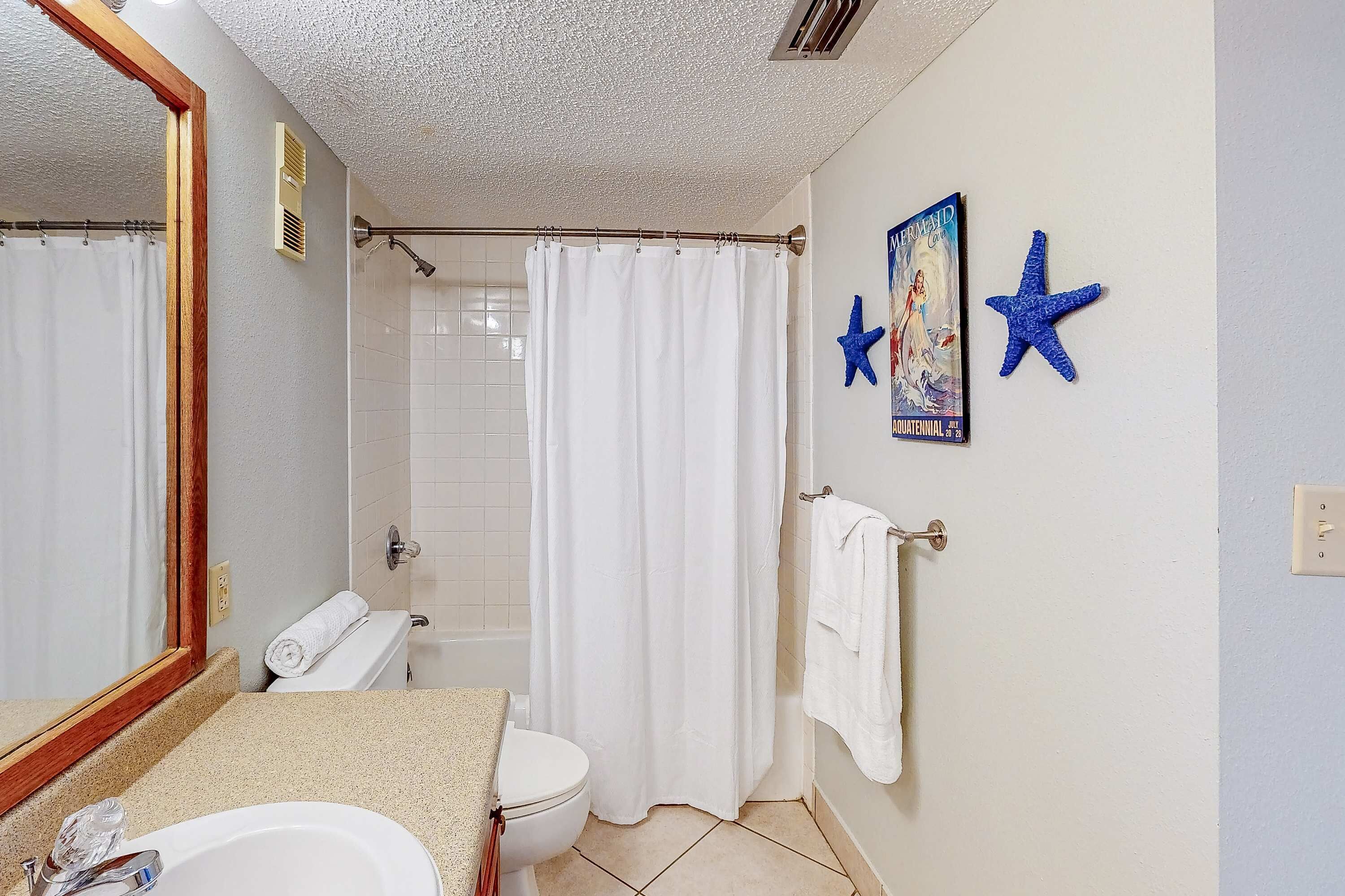 Une salle de bain avec un lavabo, des toilettes, un rideau de douche et un miroir. Deux étoiles de mer décoratives sont accrochées au mur.