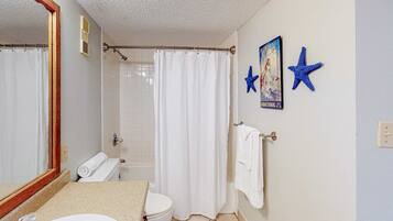 Une salle de bain avec un lavabo, des toilettes, un rideau de douche et un miroir. Deux étoiles de mer décoratives sont accrochées au mur.
