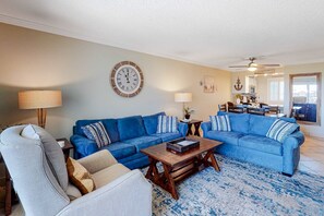 Una sala de estar con un sofá seccional azul, una mesa de centro de madera y un sillón gris.