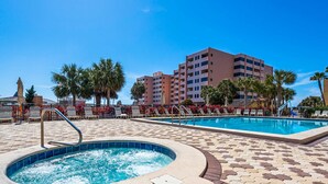 A hotel pool area with a hot tub, lounge chairs, and a palm tree-lined deck.