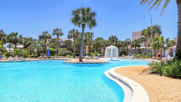 A large outdoor swimming pool with palm trees and lounge chairs around it. - Charming & sleek condo w incredible water views and shared on-site amenities (Destin)