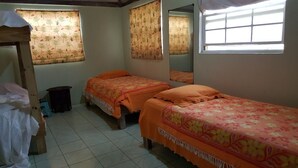 Ein Zimmer mit zwei Betten, einem Vorhangfenster, einem Spiegel und einem gefliesten Boden.