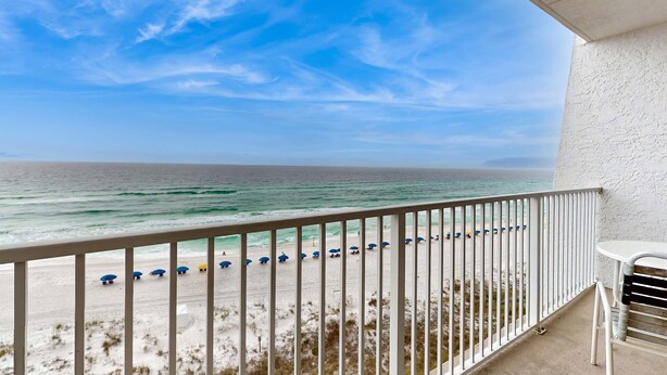 Ein Balkon mit Blick auf den Strand, mit weißer Reling und einem Tisch.