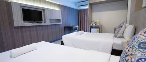 A hotel room with two beds, a TV mounted on the wall, a desk with a chair, and a small table with a lamp.