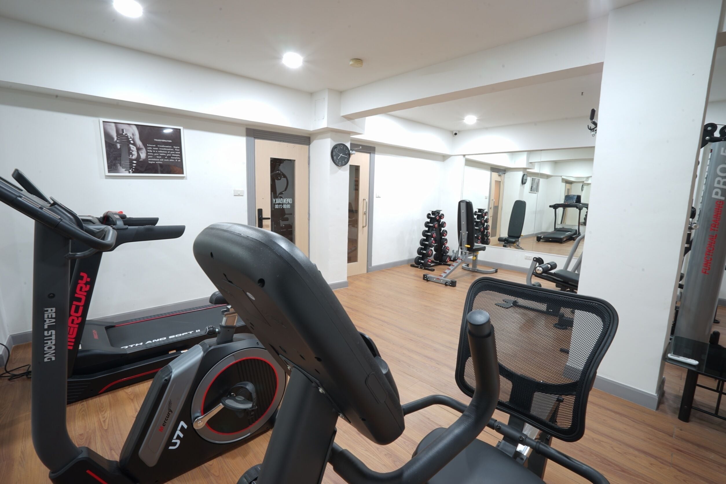 A gym with exercise equipment, a mirror, and a clock on the wall.