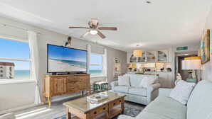 Una sala de estar con televisor, ventilador de techo, sofá, mesa de centro y vista a la playa.