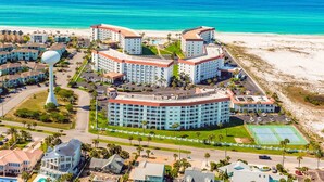 Un complejo hotelero frente al mar con varias construcciones, una torre blanca destacada y vistas a la playa.
