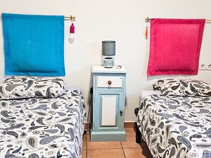 Deux lits avec une literie à motifs, une petite table de chevet avec une lampe et un luminaire fixé au mur.